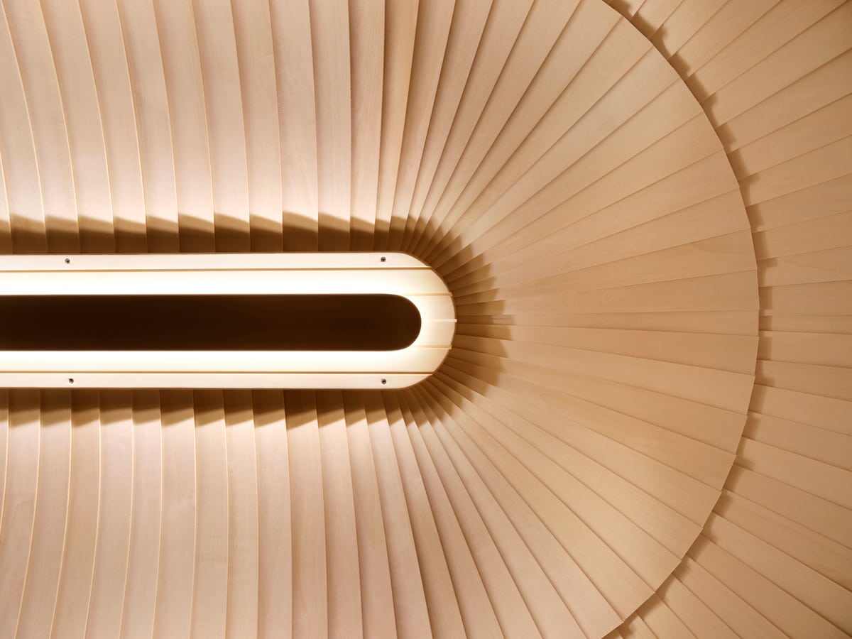 Curved wooden sauna ceiling with warm lighting following its rounded shape.